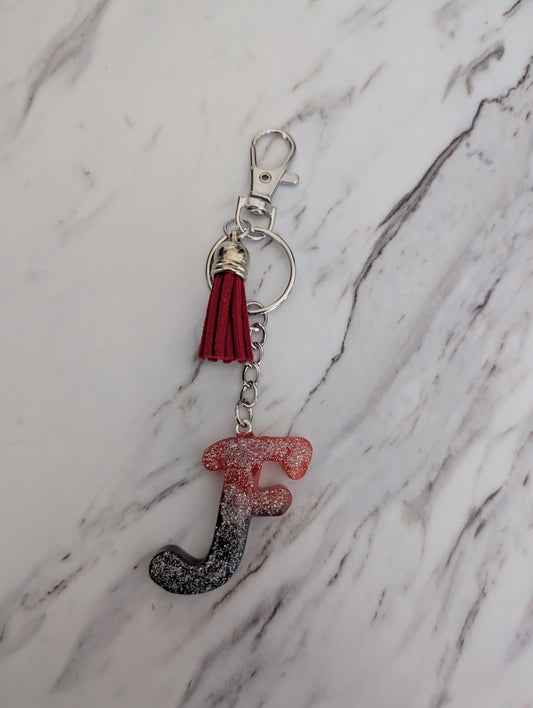 Keychain with letter 'F' and red tassel on a marble background