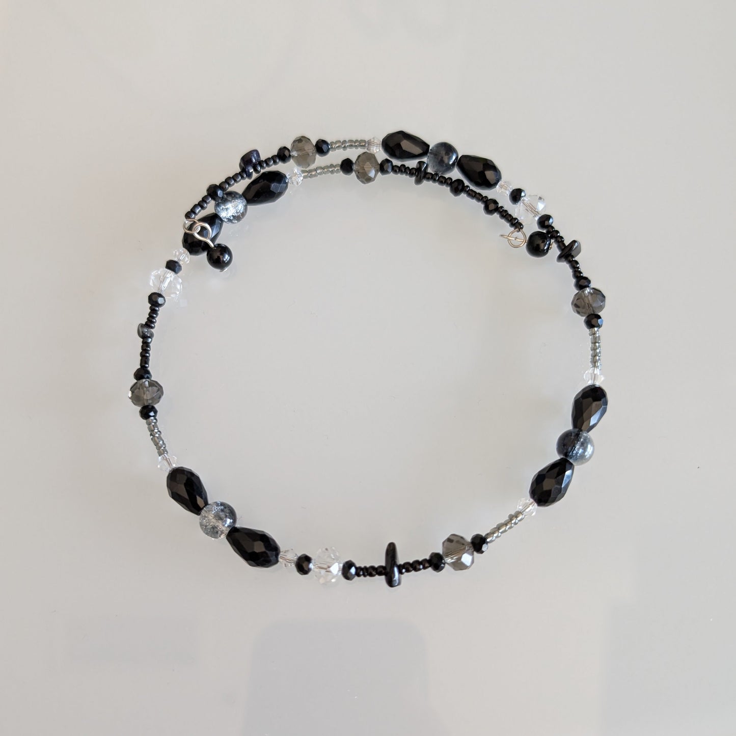 Modern minimalist choker necklace featuring a linear arrangement of black glass beads and faceted smoke-grey crystals on a flexible silver-tone coil.