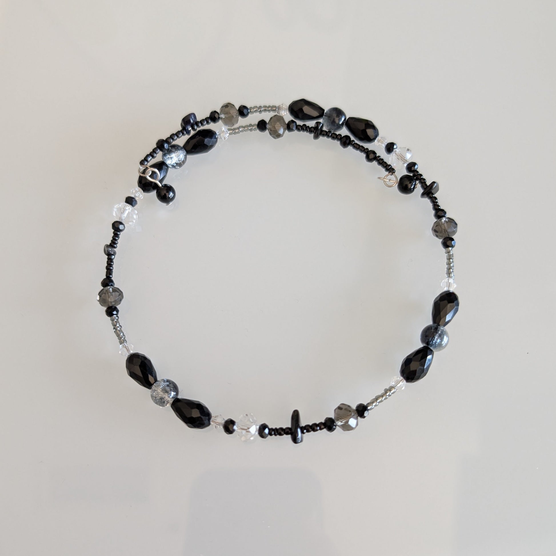 Modern minimalist choker necklace featuring a linear arrangement of black glass beads and faceted smoke-grey crystals on a flexible silver-tone coil.