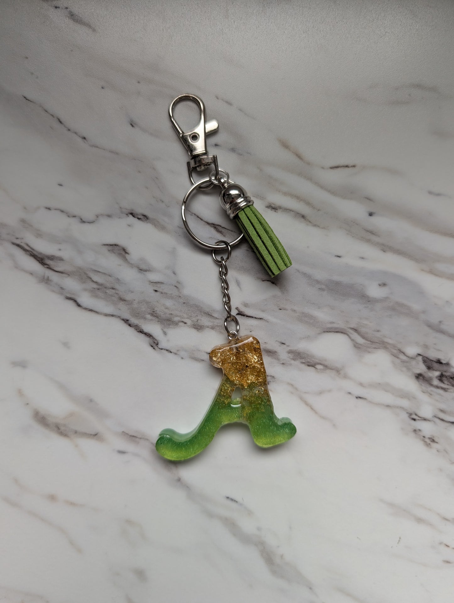 Green and gold letter A keychain on a marble surface