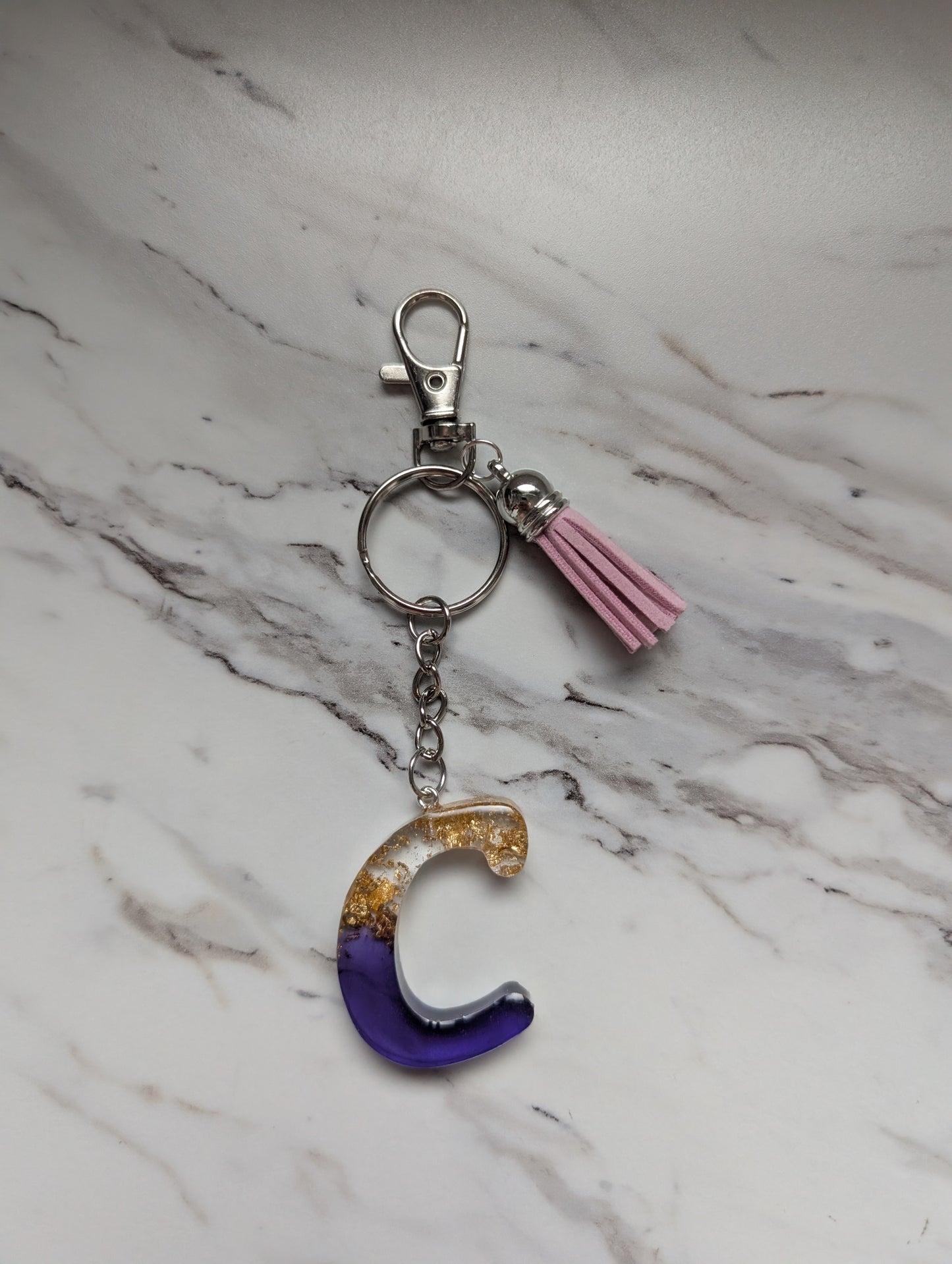 Gold and purple Keychain with letter 'C' and tassel on a marble surface