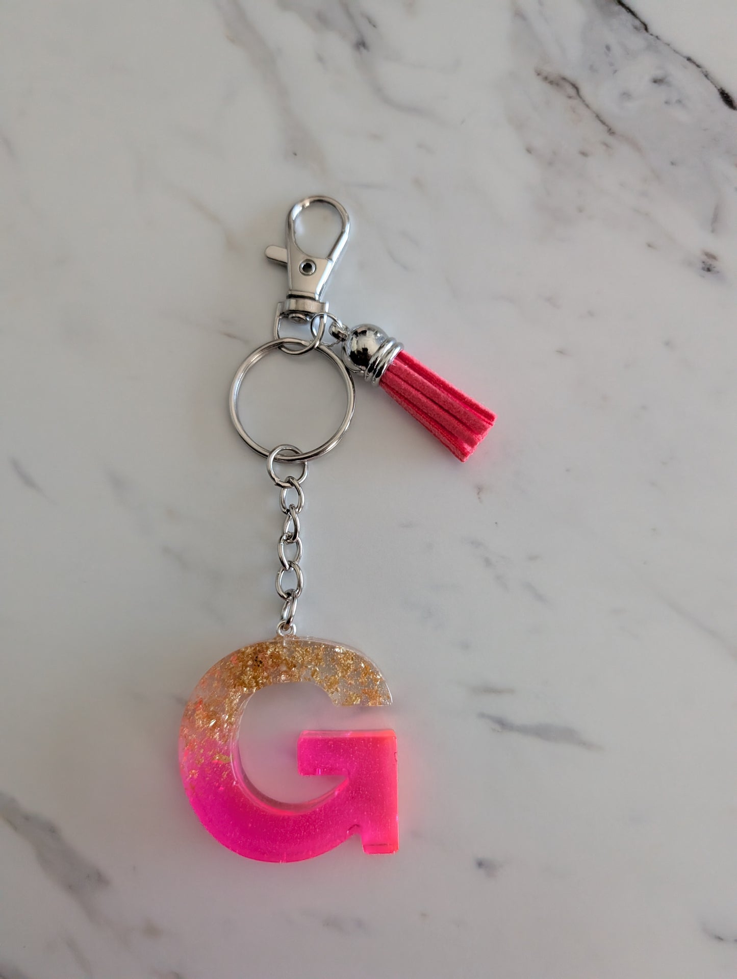 Keychain with pink letter 'G' and tassel on a marble background