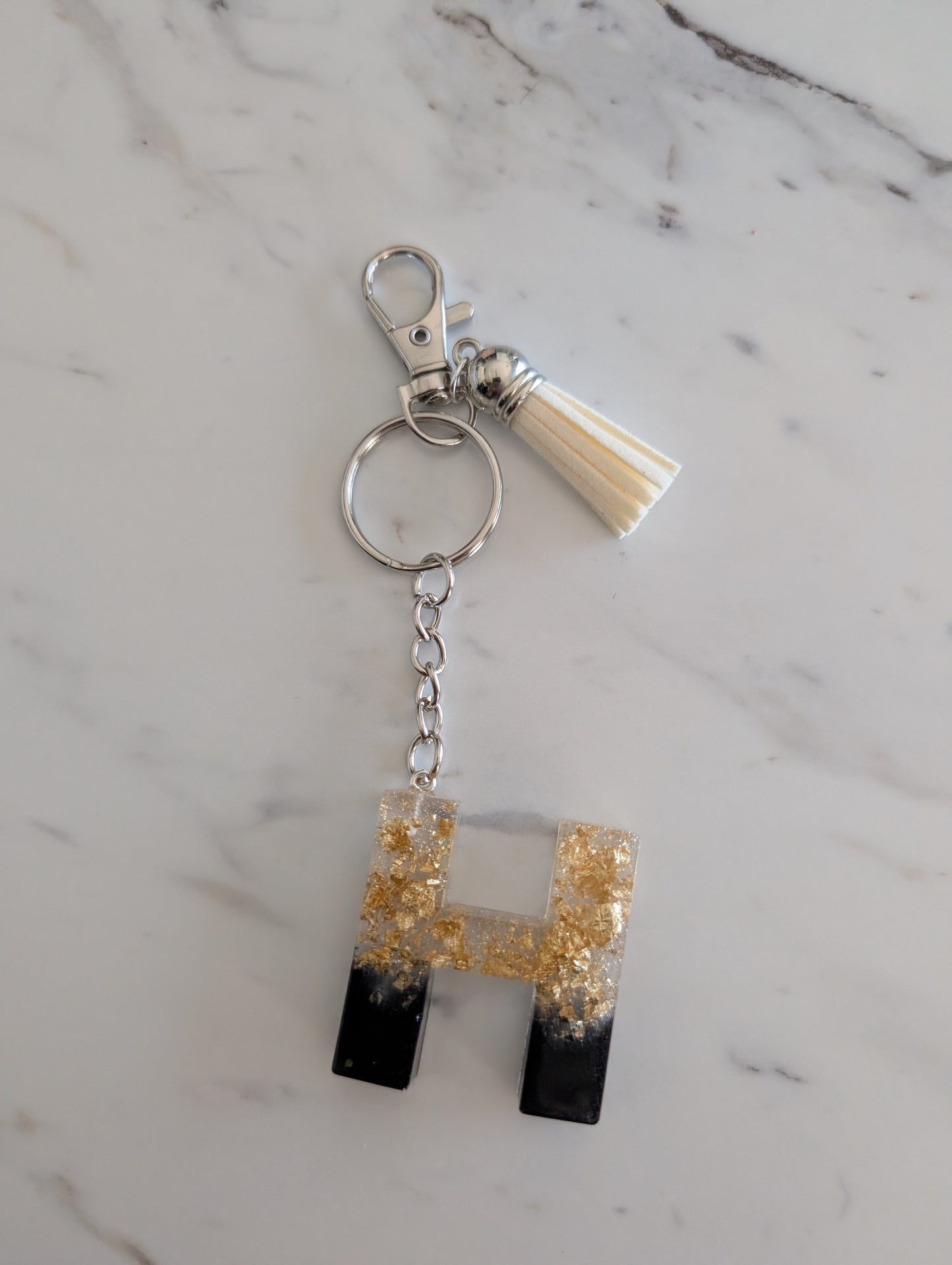 Gold and black Keychain with letter 'H' design on a marble surface