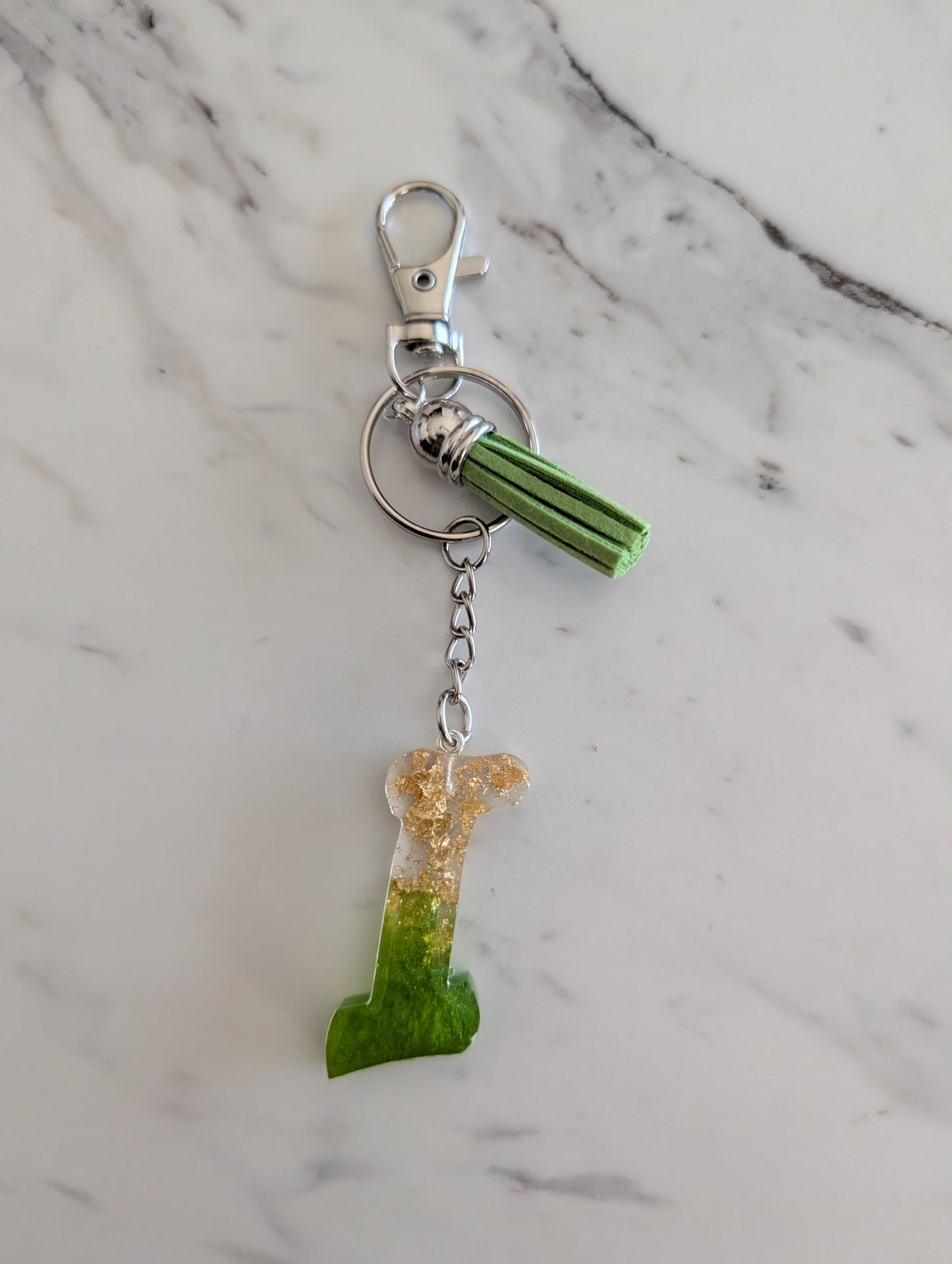 Gold and green letter I Keychain on a marble surface