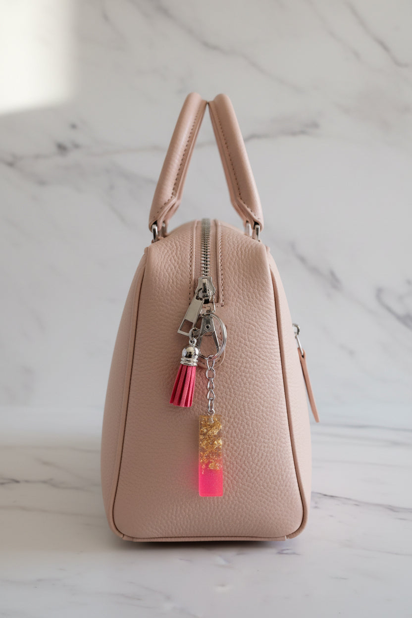 Pink handbag with a gold and hot Pink letter I keychain on a marble surface