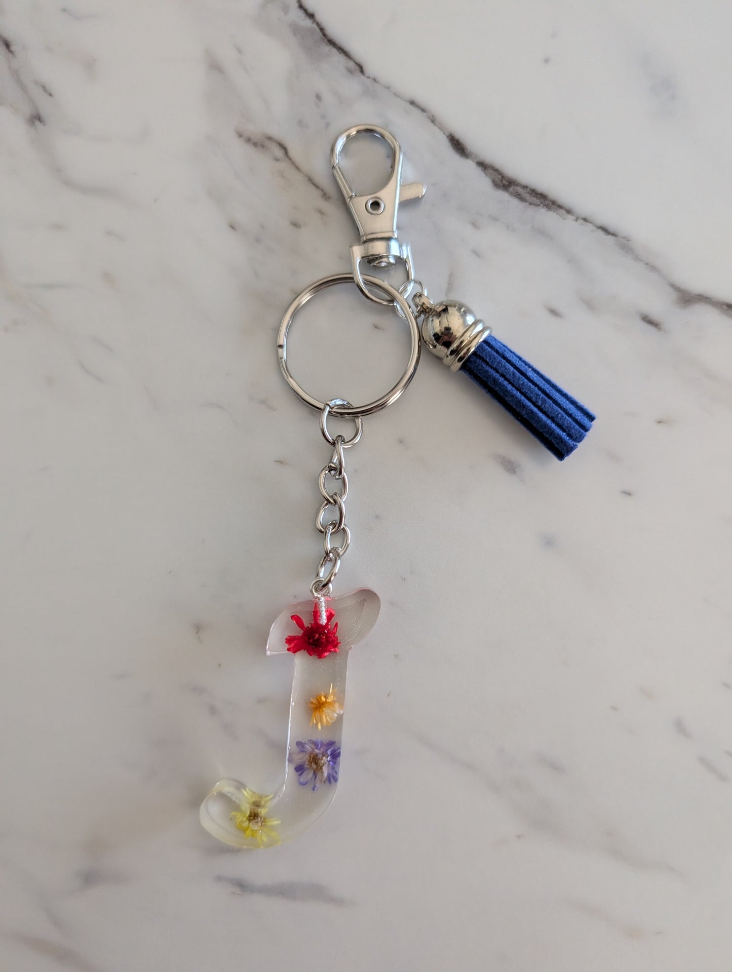 Keychain with tassel and floral letter J charm on a marble surface