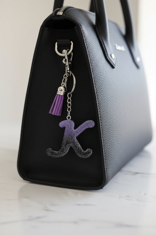 Black handbag with a keychain featuring a letter 'K' and purple accent on a marble surface.