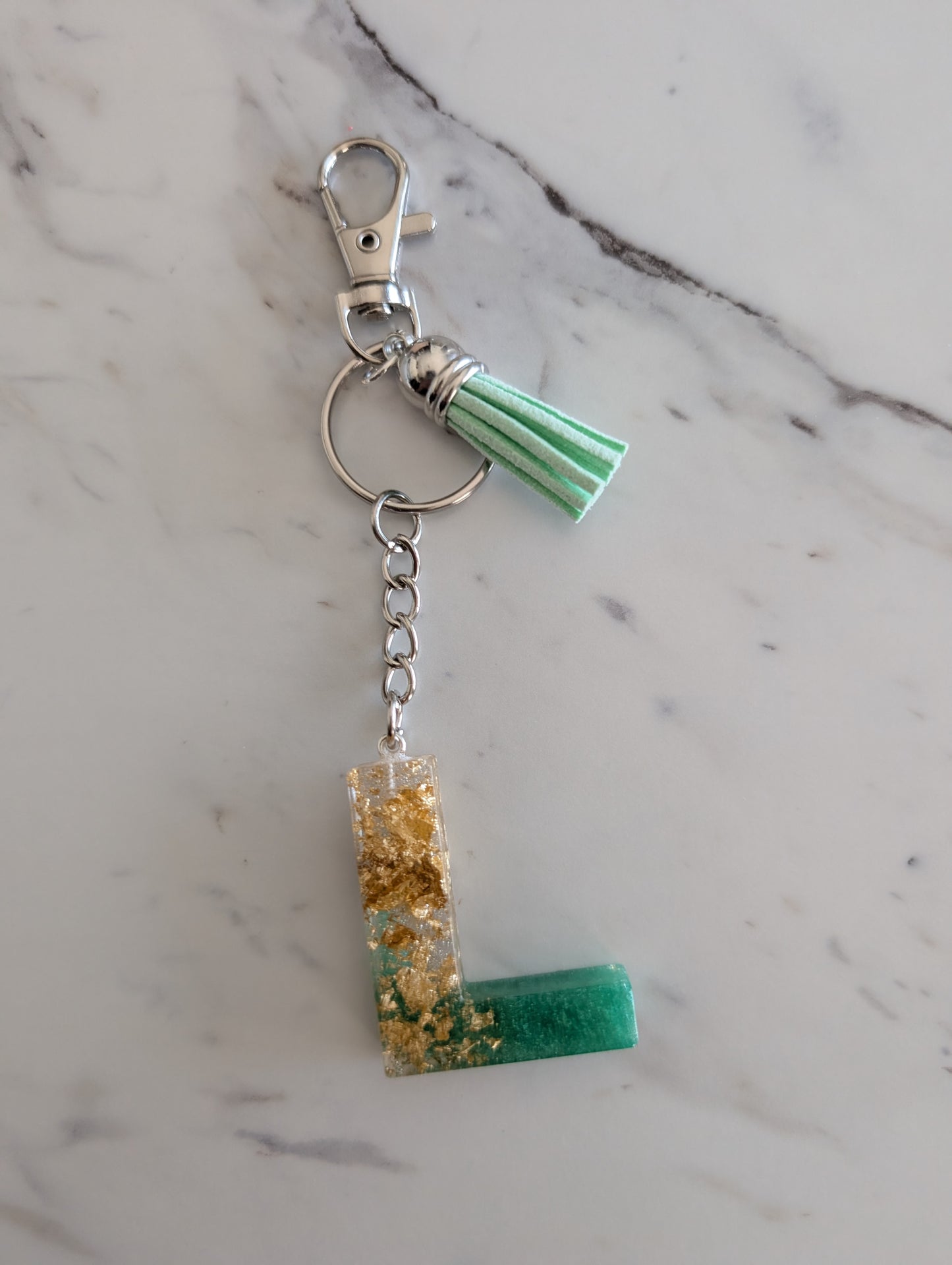 Keychain with green and gold letter L design on a marble surface