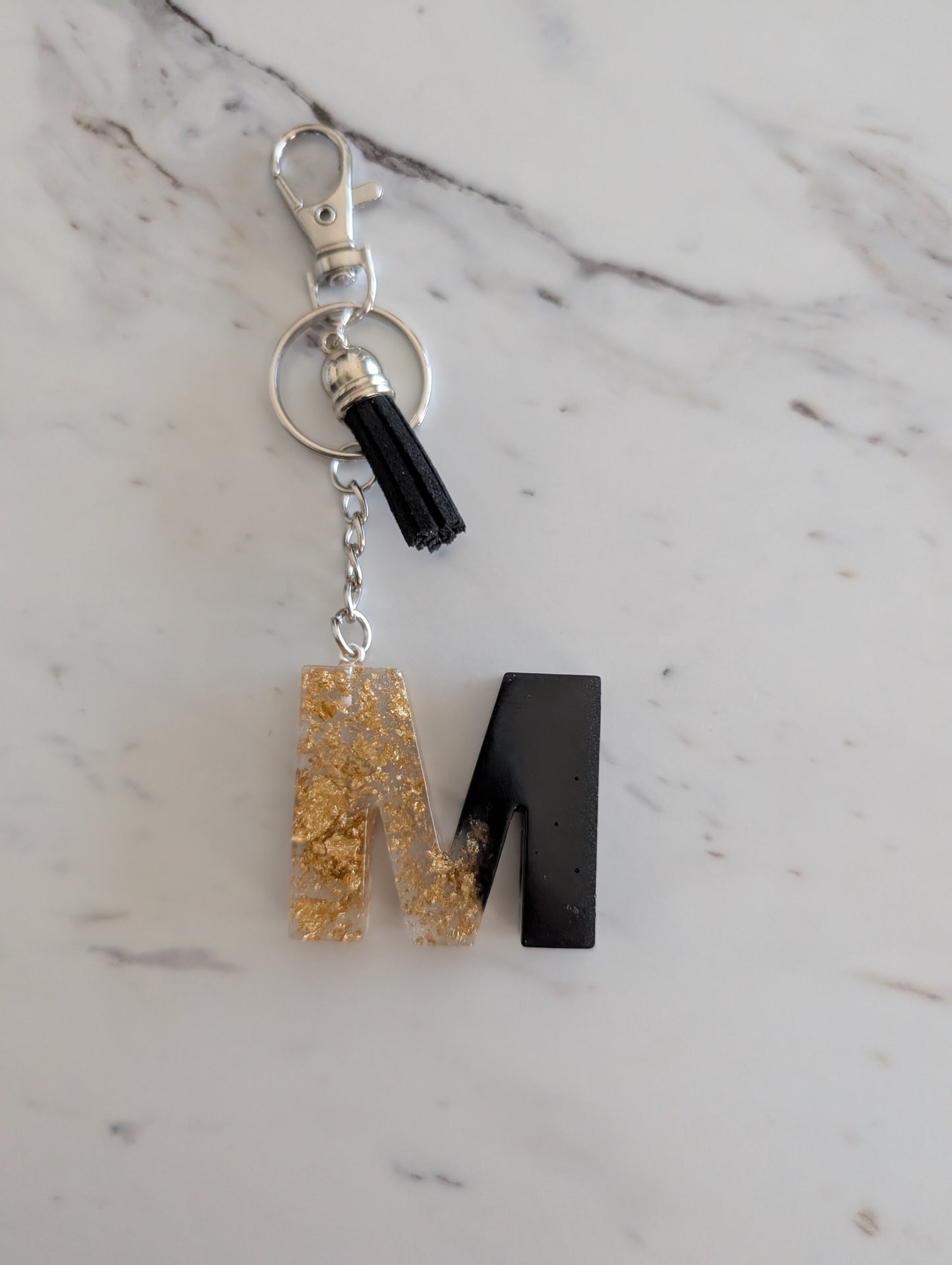 Gold and black Keychain with letter 'M' on a marble surface