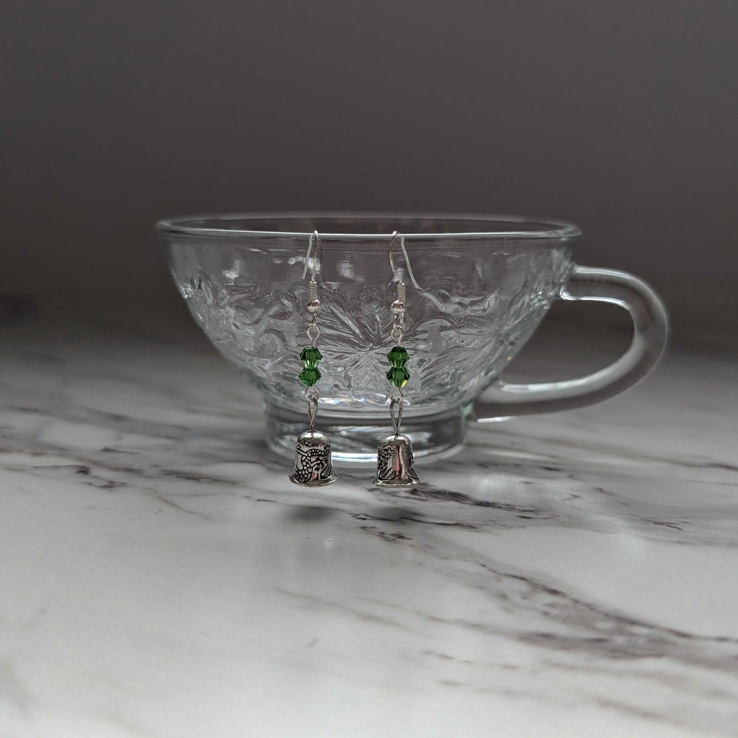 Clear glass teacup with earrings on a marble surface