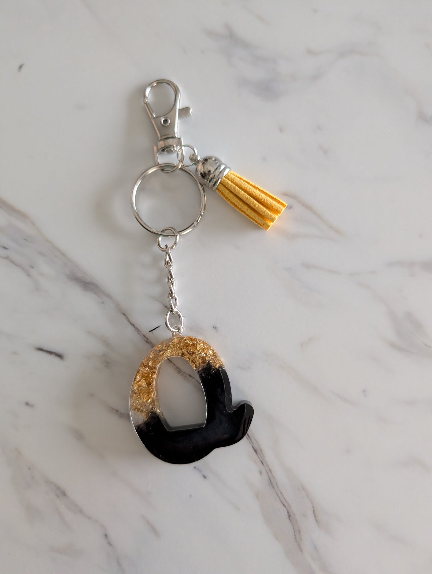 Keychain with black and gold letter Q on a marble surface
