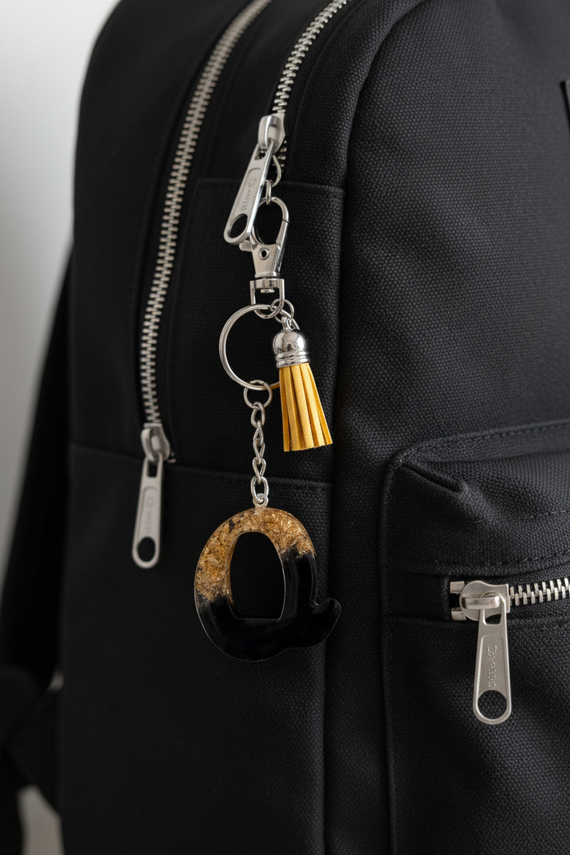 Keychain with black and gold letter Q design on a black bag