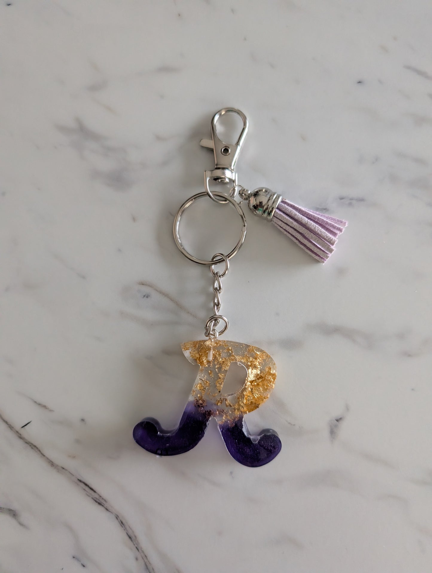 Gold and purple Keychain with letter 'R' charm on a marble surface