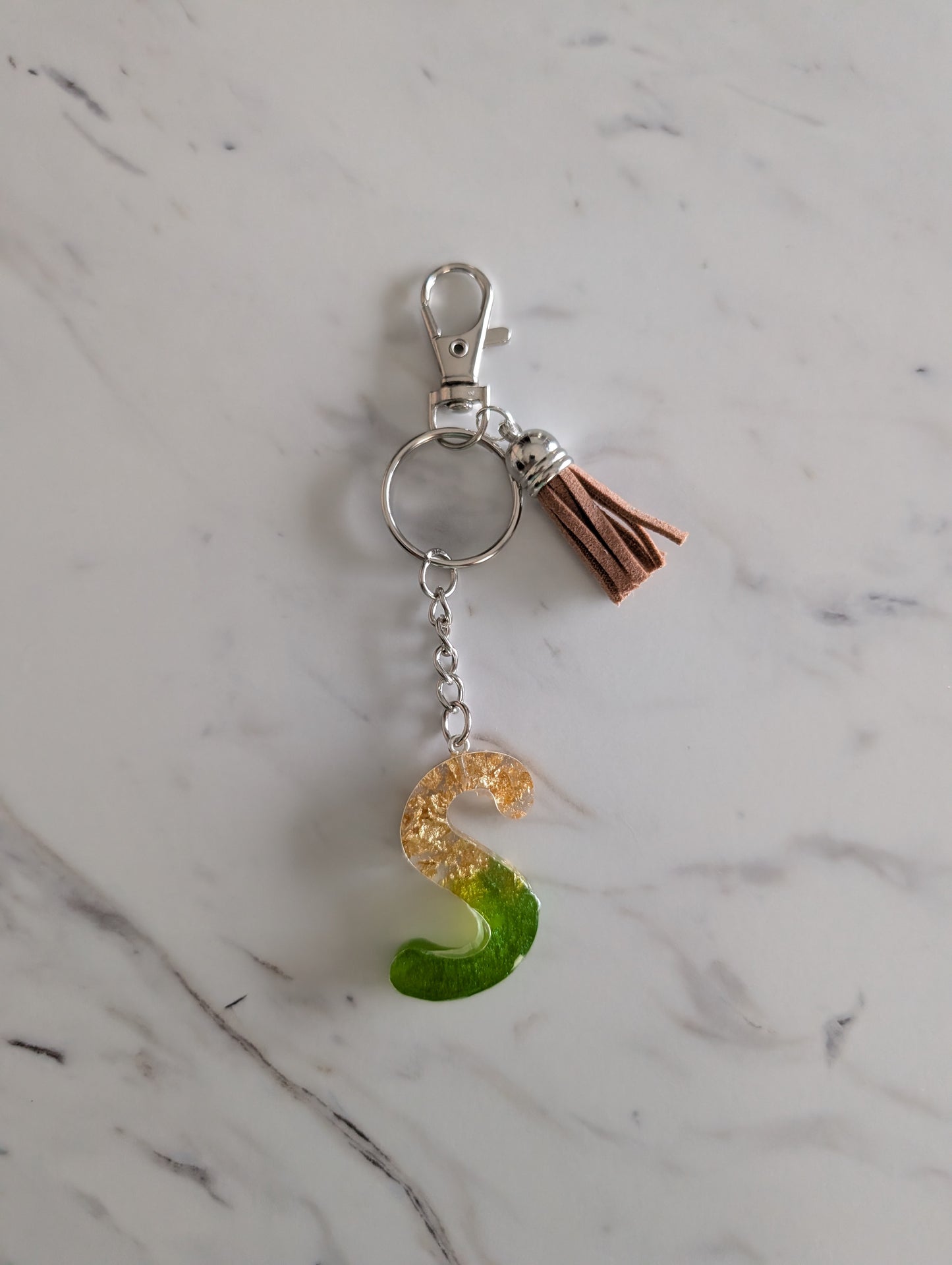 Gold and green Keychain with letter 'S' charm on a marble surface