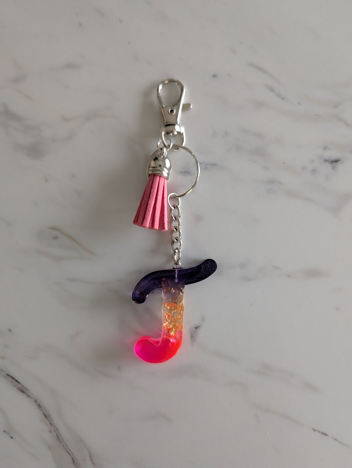 Colorful Letter T keychain charm with a pink tassel on a marble surface