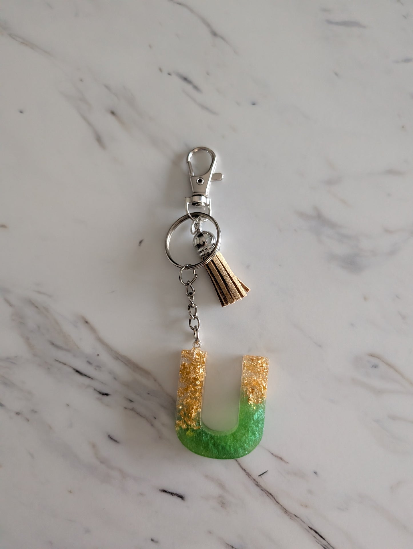 Letter U Keychain with green and gold design on a marble surface