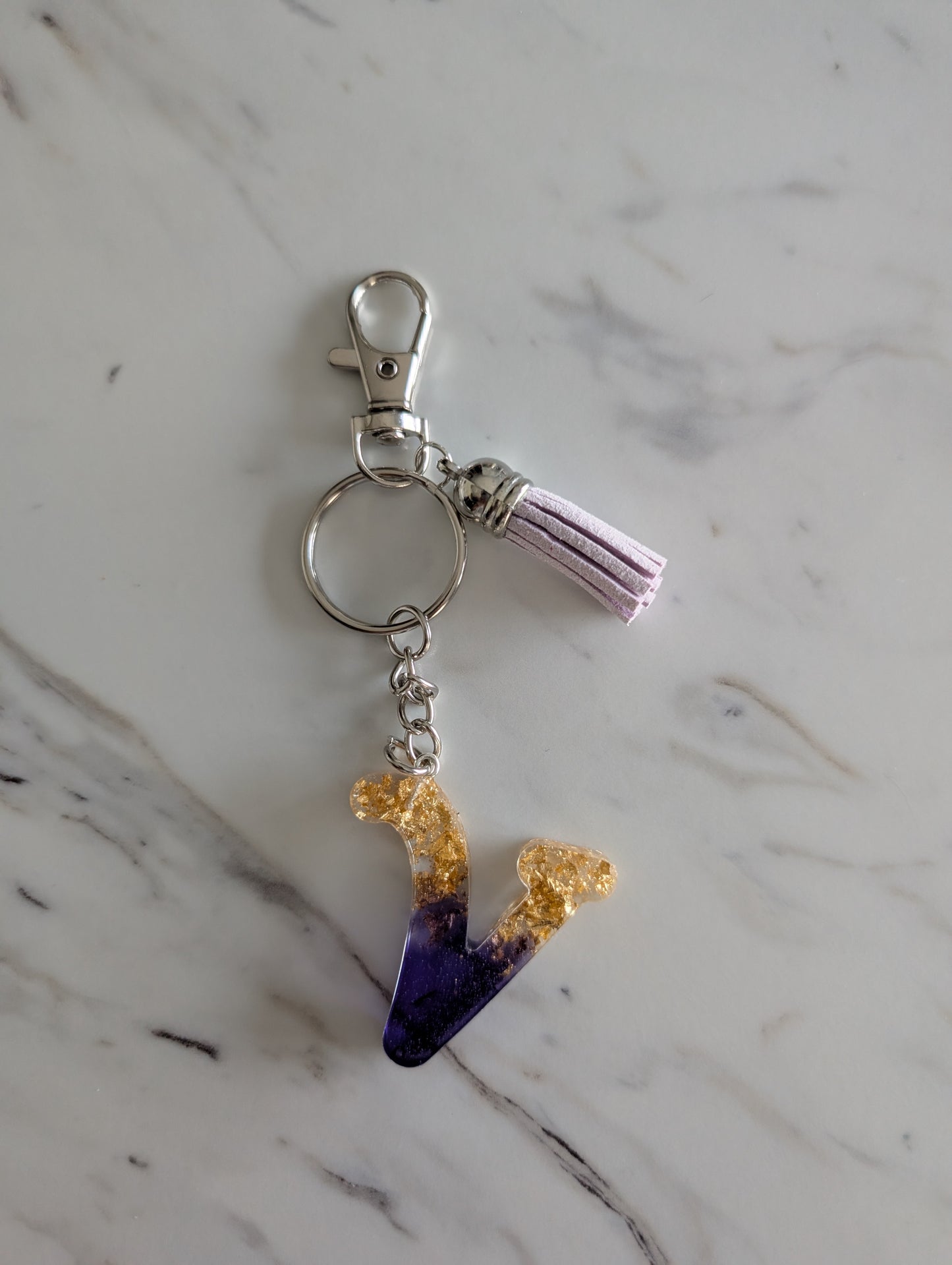 Gold and purple letter V Keychain on a marble surface