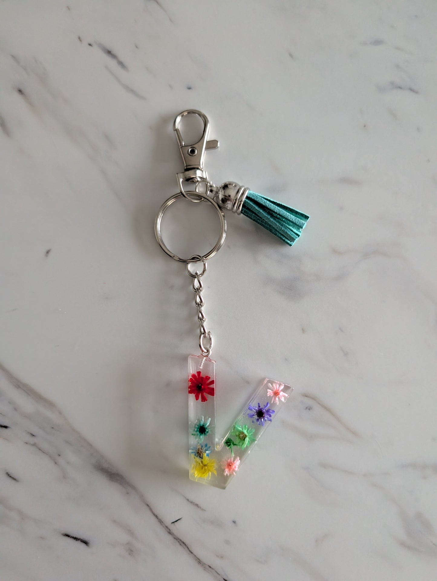 Letter V Keychain with colorful flowers and a tassel on a marble surface