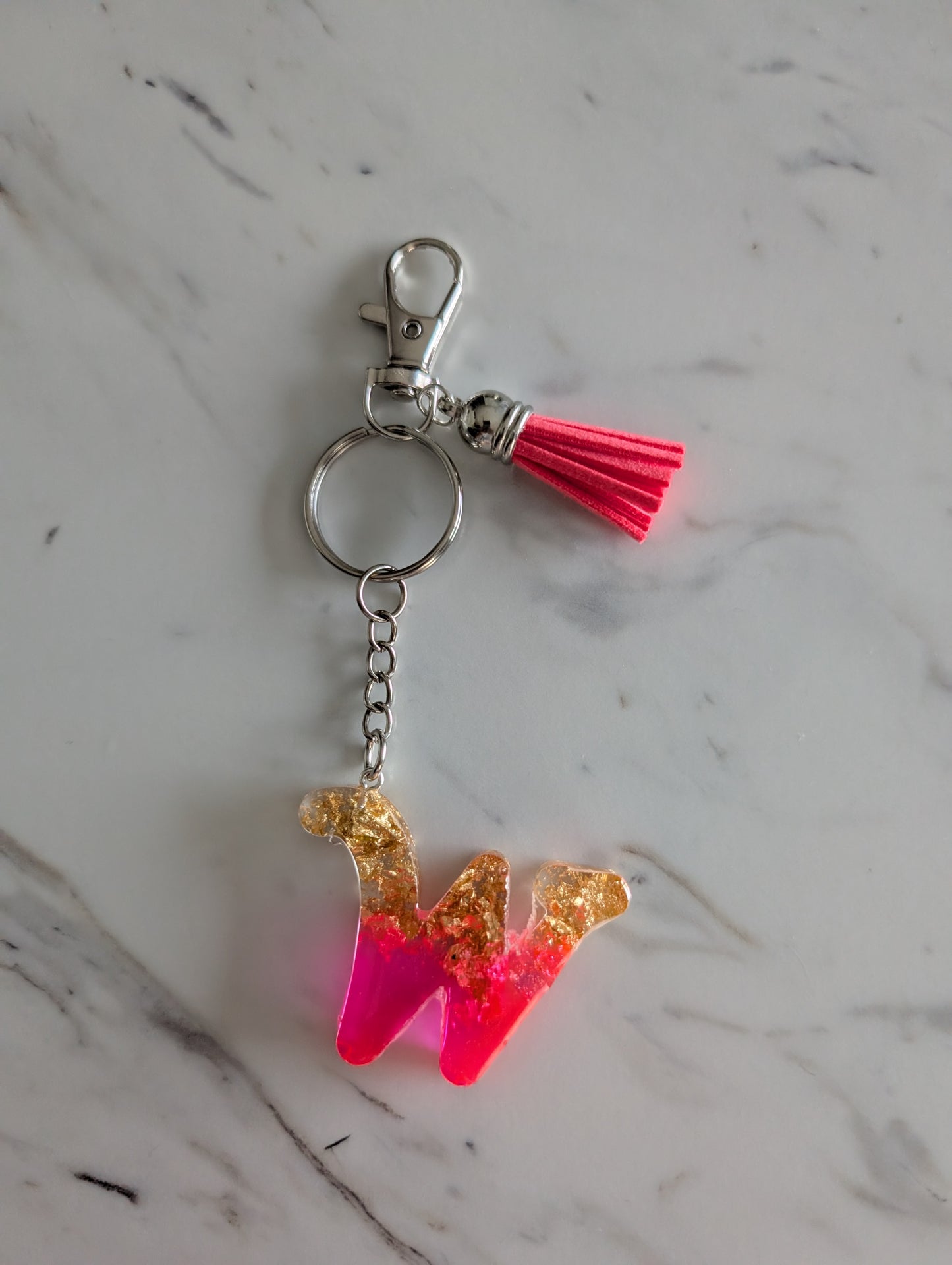 Keychain with pink and gold letter 'W' charm on a marble surface