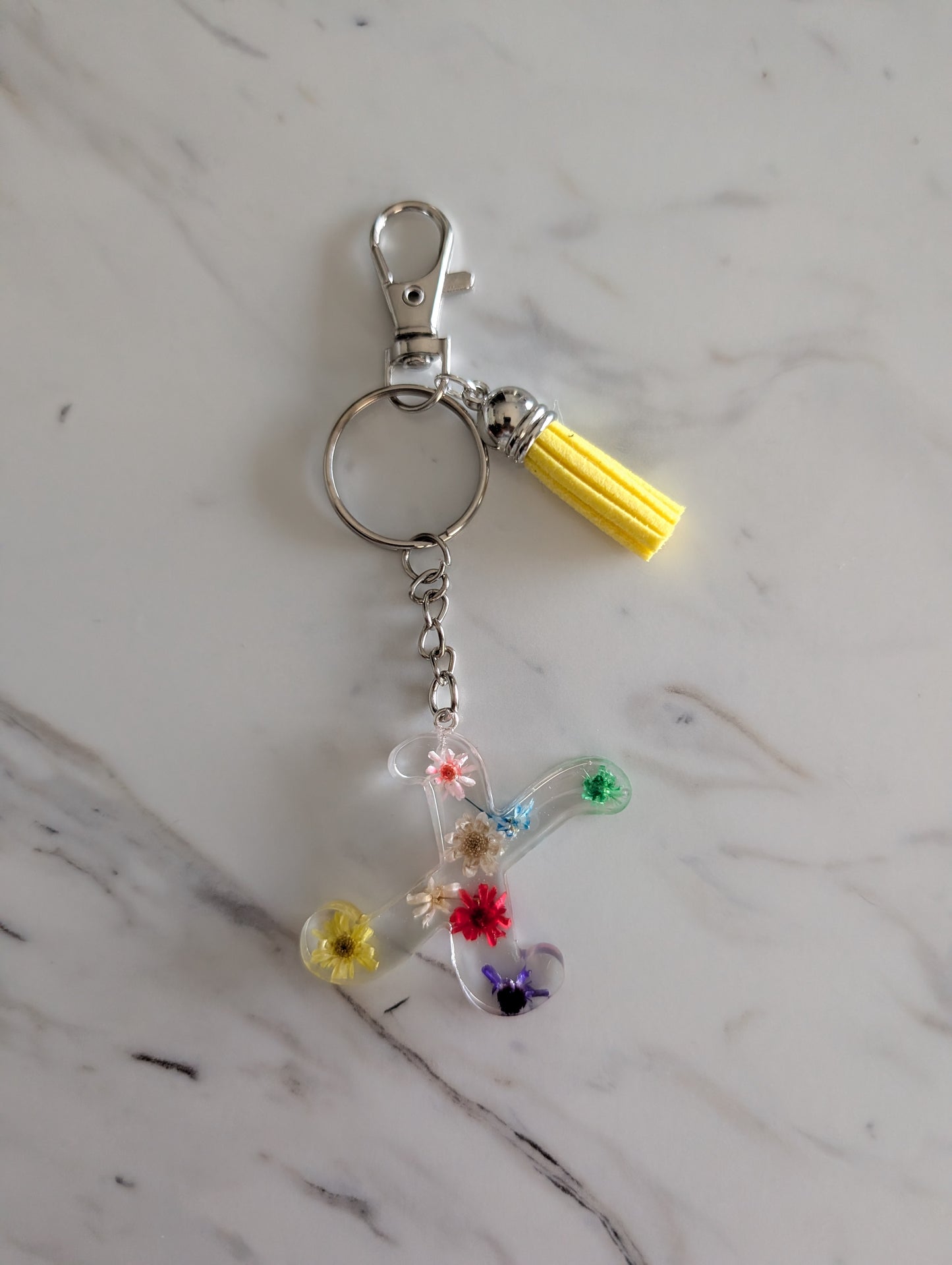 Letter X Keychain with floral design and yellow tassel on a marble surface
