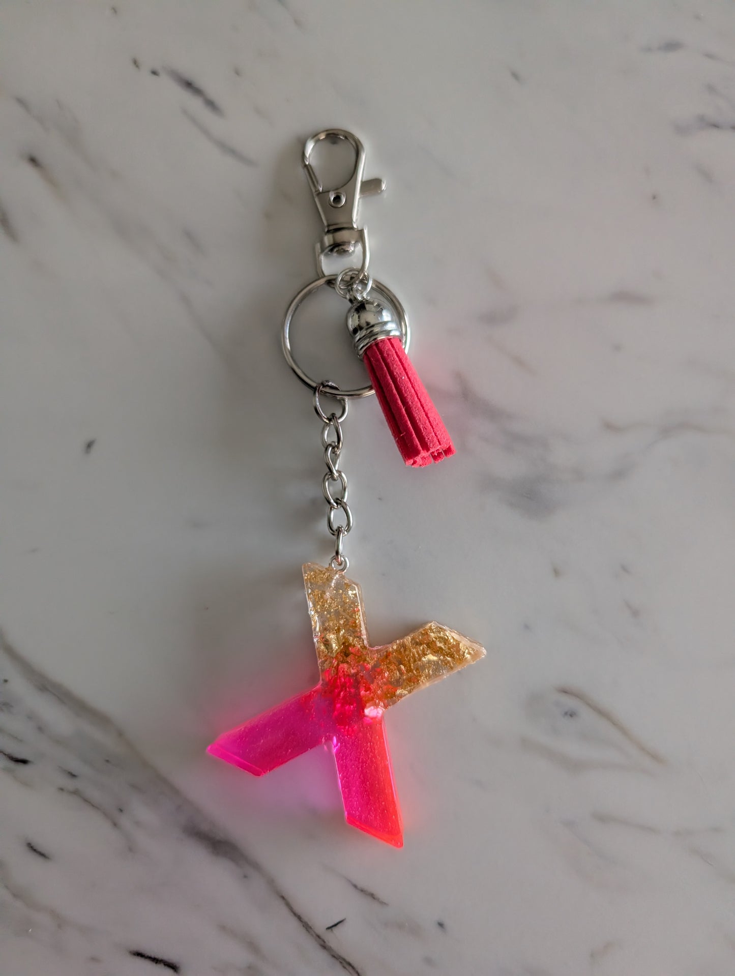 gold and pink Letter X Keychain  on a marble surface