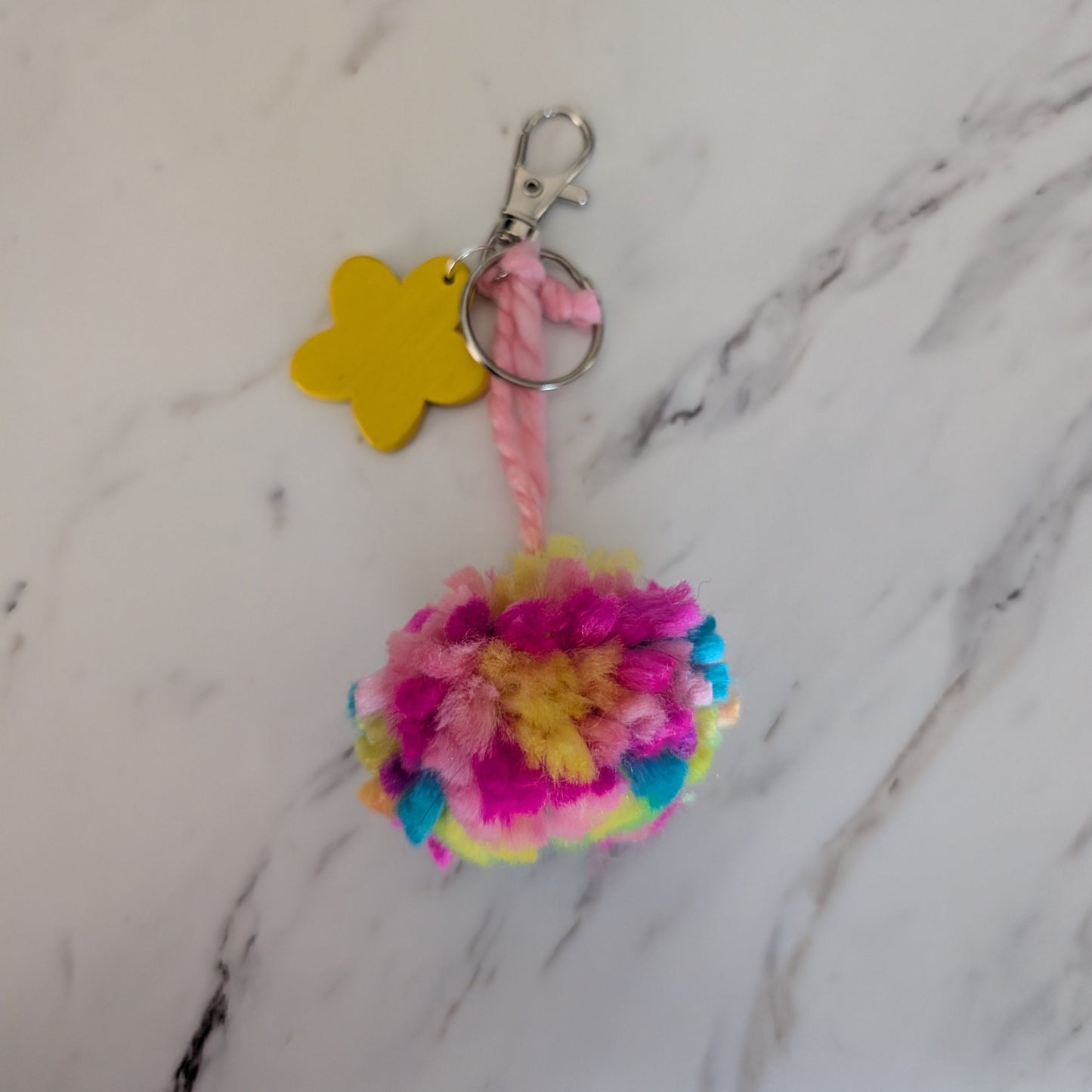 Colorful pom-pom keychain with a star-shaped tag on a marble surface