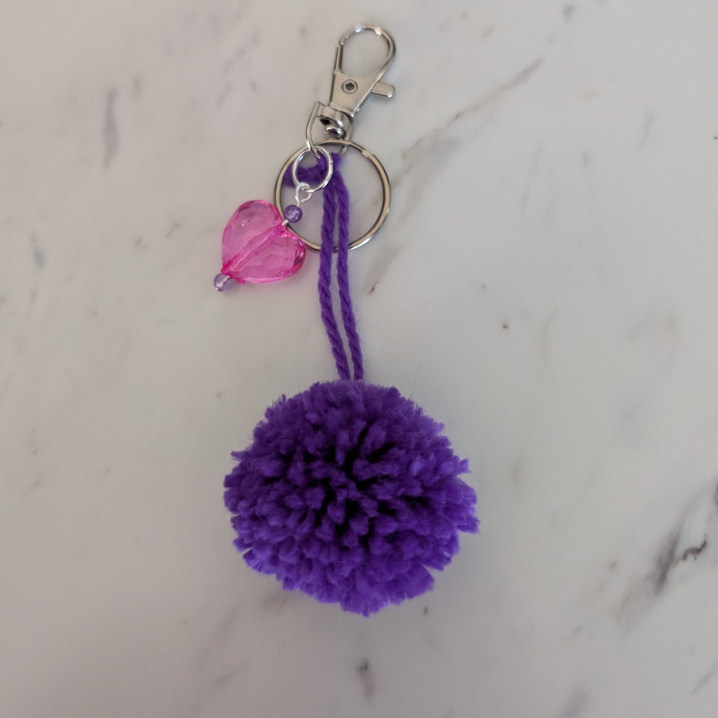 Purple pom-pom keychain with a pink heart charm on a marble background