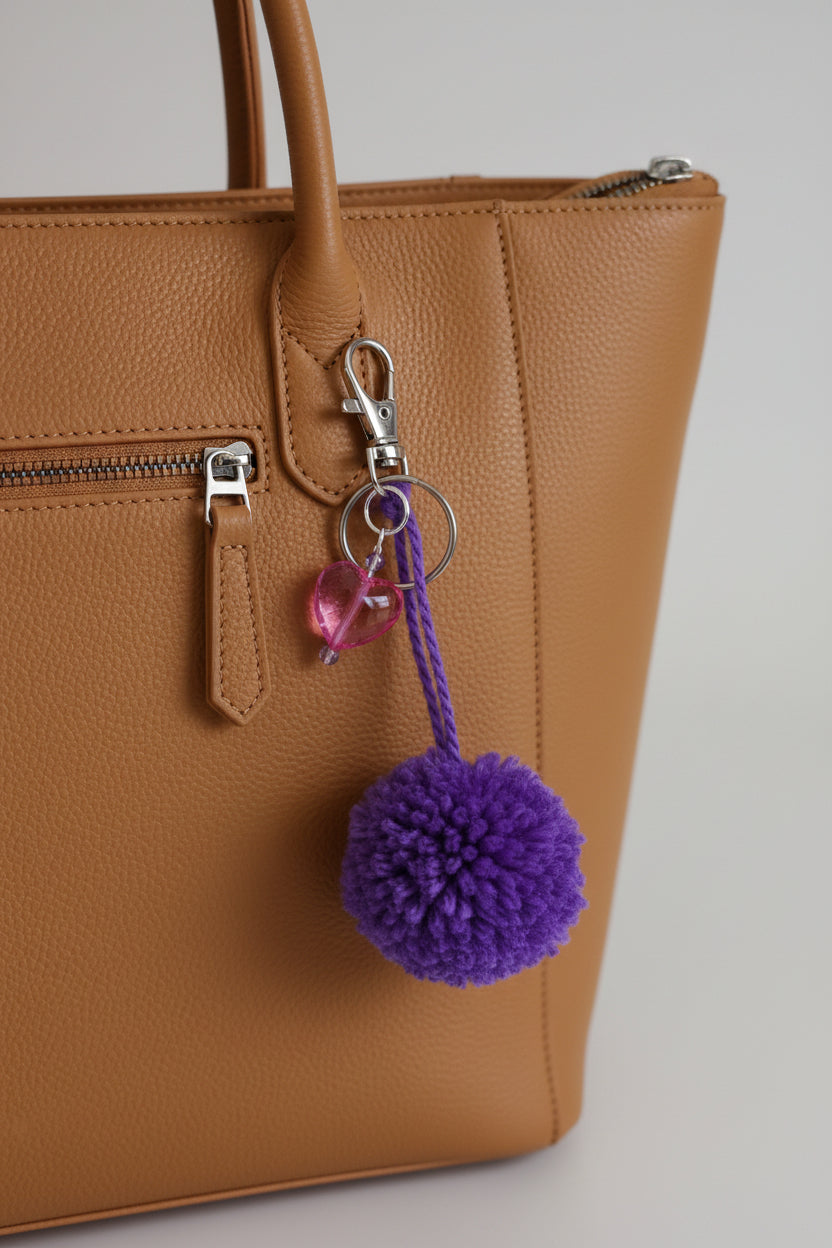 Purple pom-pom keychain with a pink heart charm on a bag