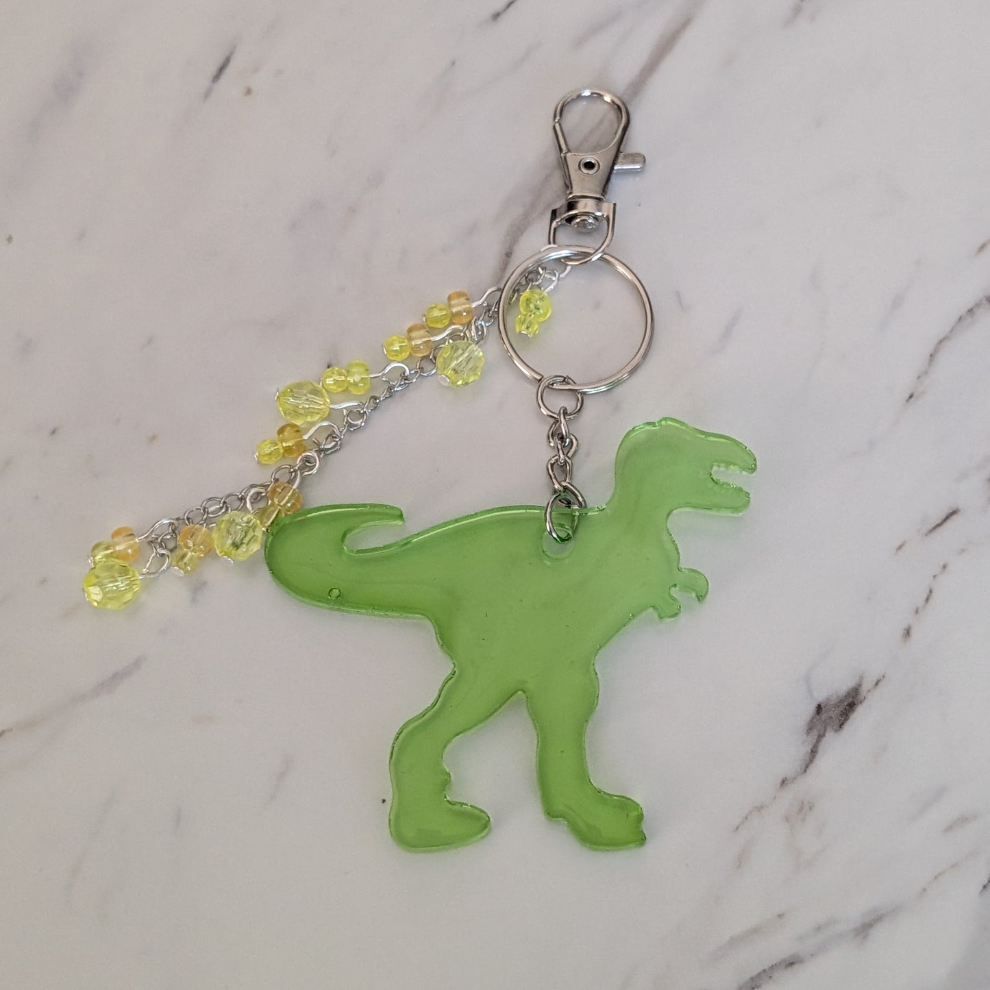 Green dinosaur keychain with yellow beads on a marble background