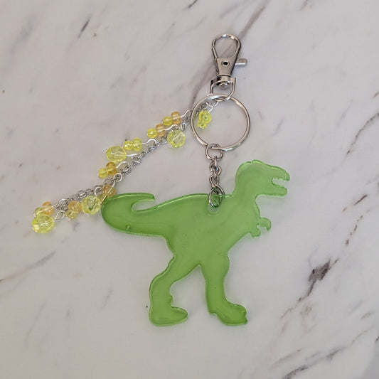 Green dinosaur keychain with yellow beads on a marble background