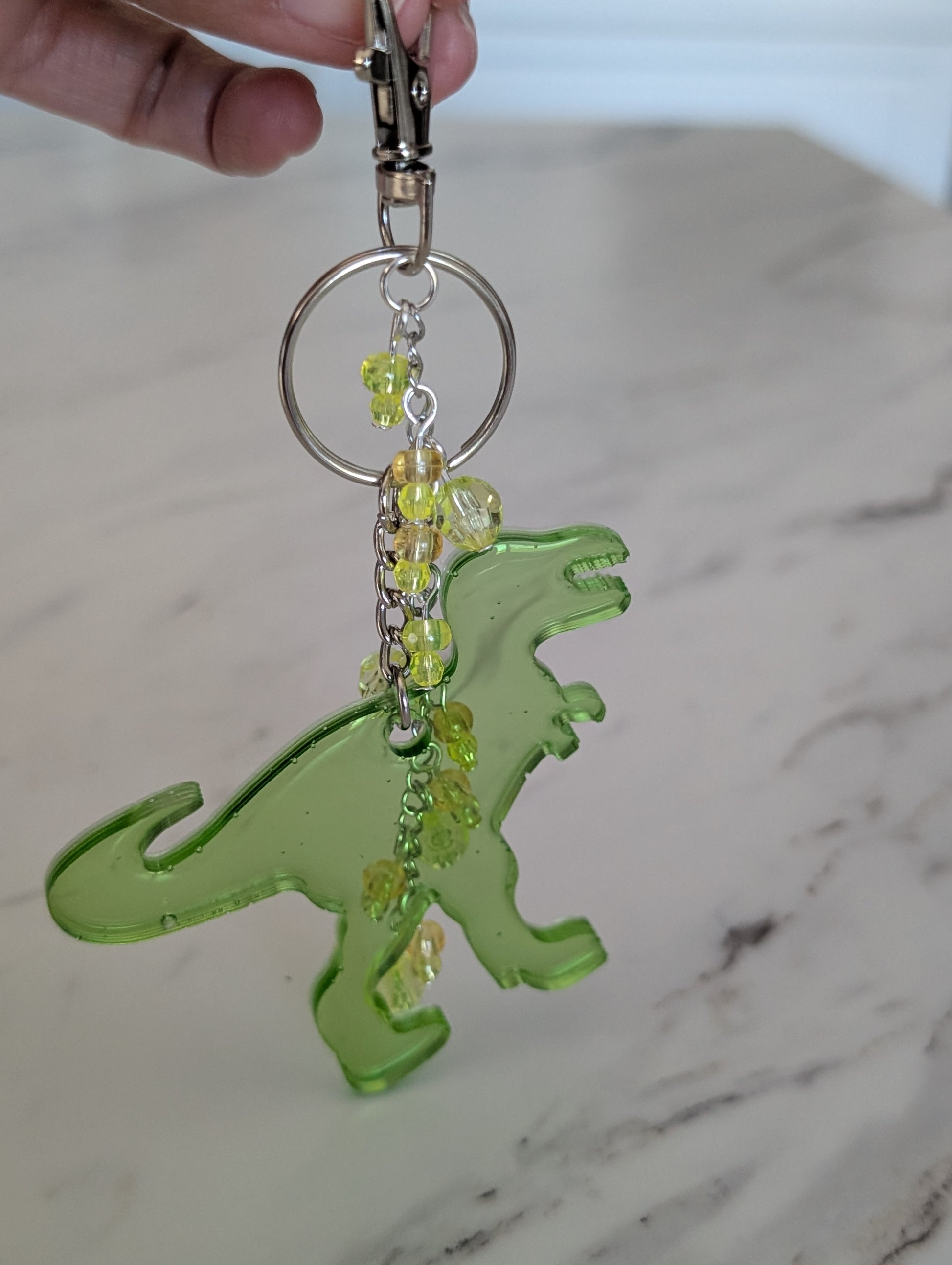 Green dinosaur keychain with beads on a marble surface