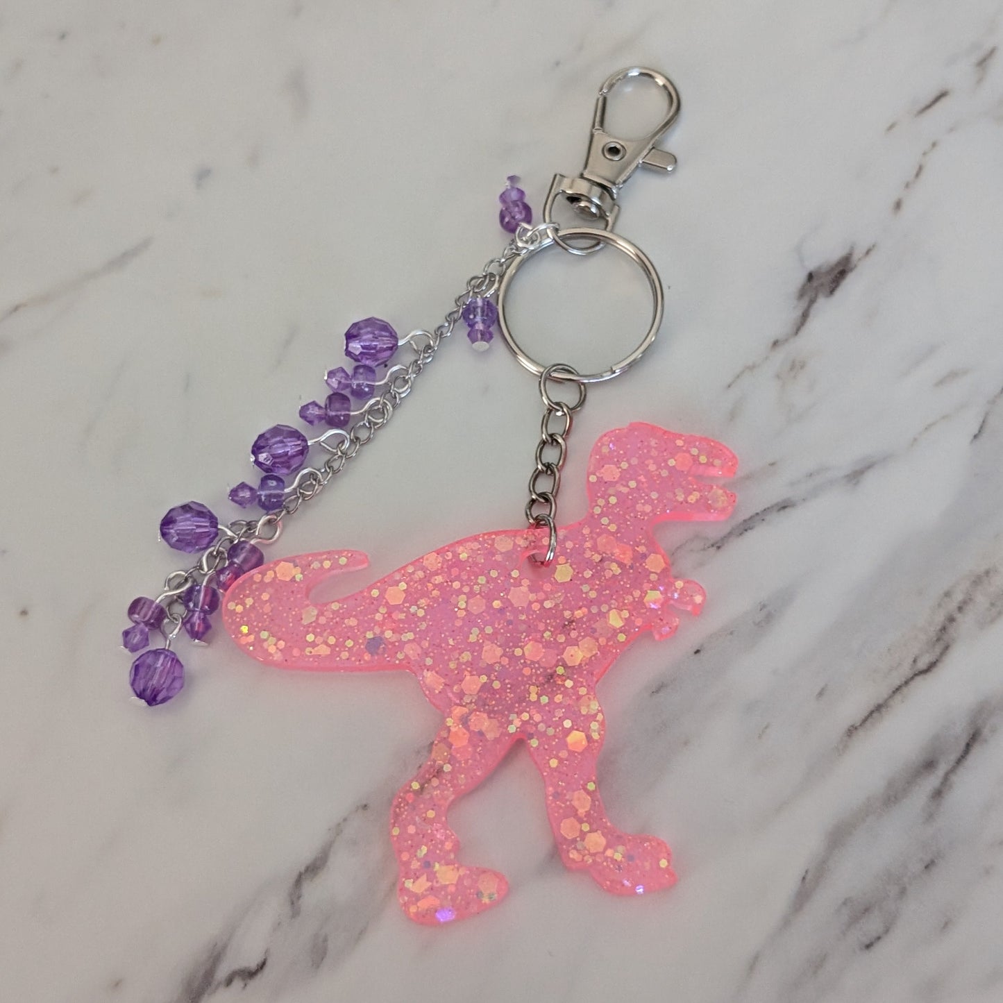 Pink glittery fairy keychain with purple beads on a marble background