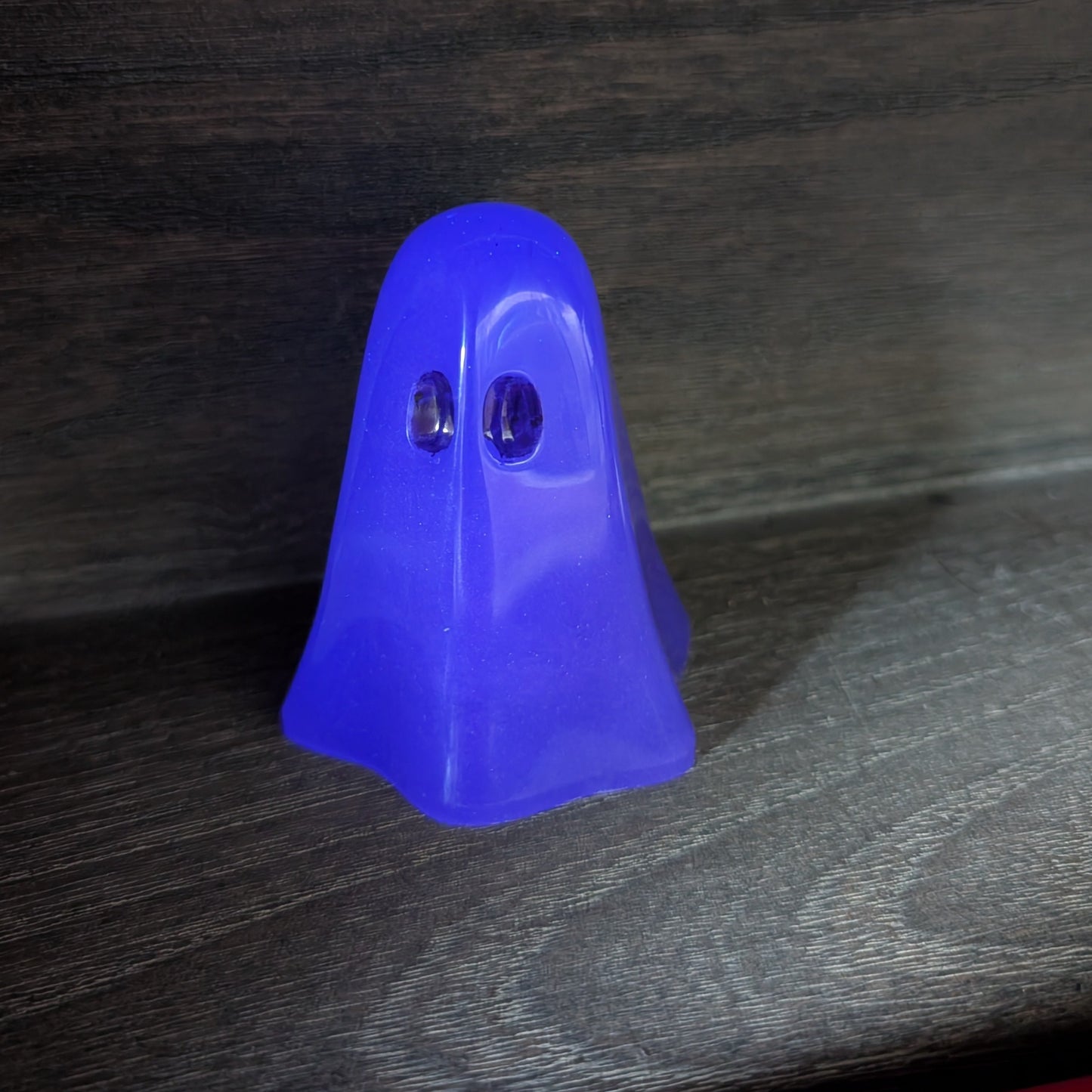 Handcrafted purple resin ghost figurine standing upright with dark eye and mouth details on a wooden surface.