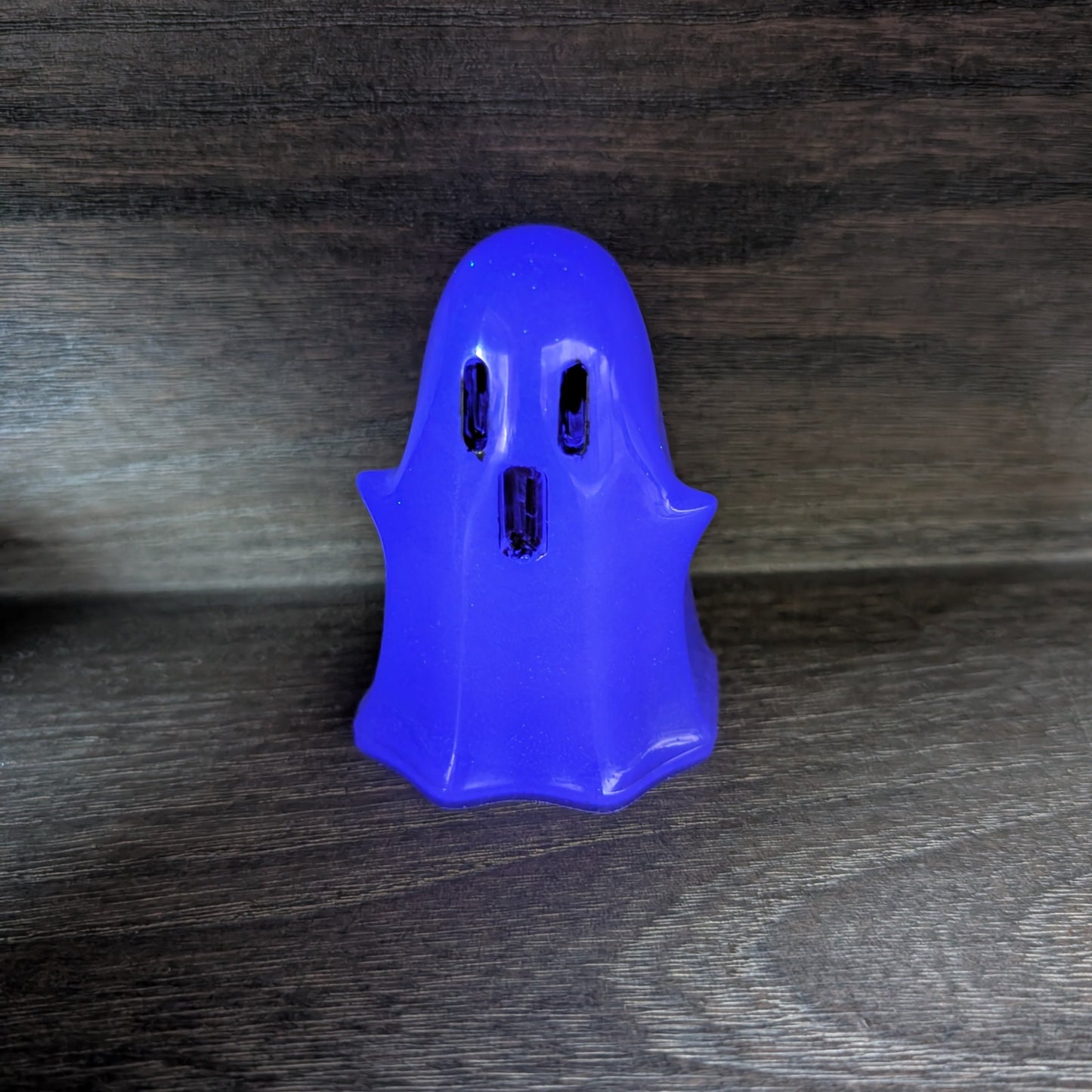 Handcrafted purple resin ghost figurine standing upright with dark eye and mouth details on a wooden surface.