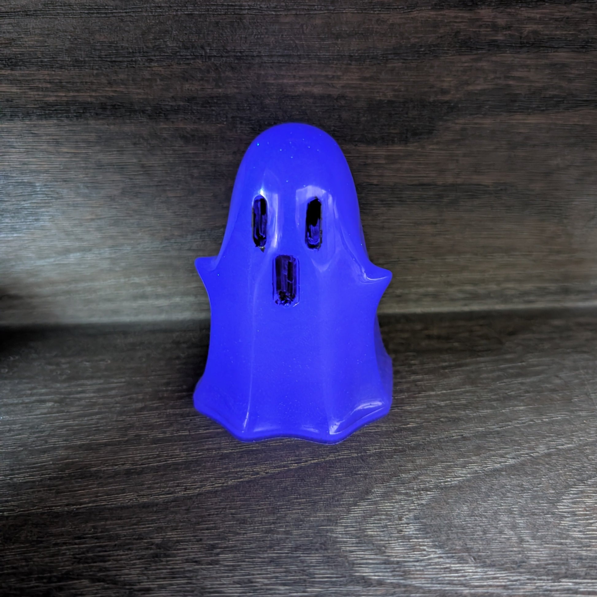 Handcrafted purple resin ghost figurine standing upright with dark eye and mouth details on a wooden surface.