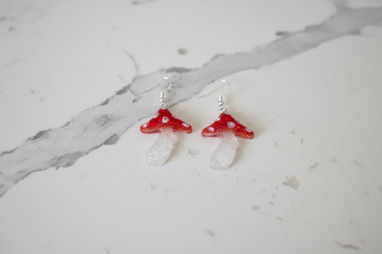 Mushroom-shaped earrings with red caps and clear stems on a dark surface