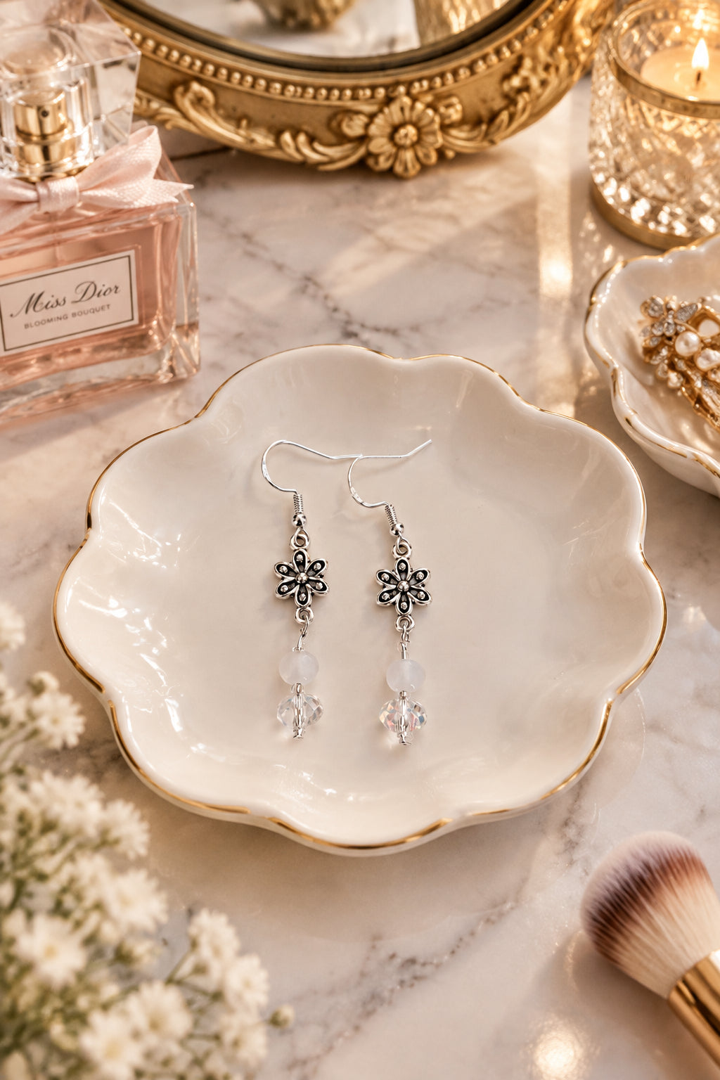 A pair of silver dangle earrings with floral charms, clear faceted beads, and iridescent white beads.