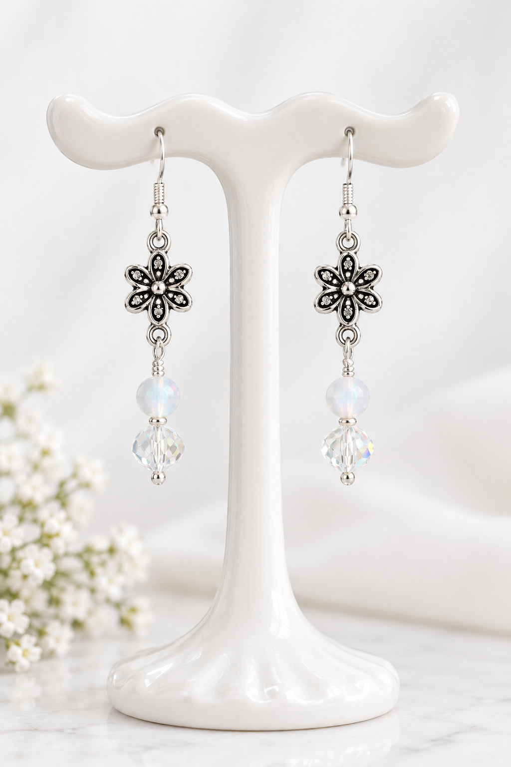 A pair of silver-toned dangle earrings with flower-shaped charms, round white beads, and clear faceted beads.