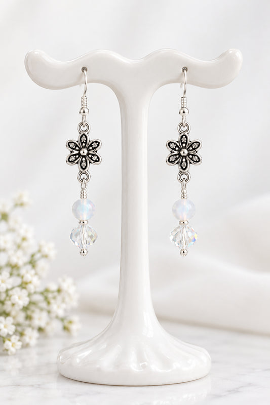 A pair of silver-toned dangle earrings with flower-shaped charms, round white beads, and clear faceted beads.