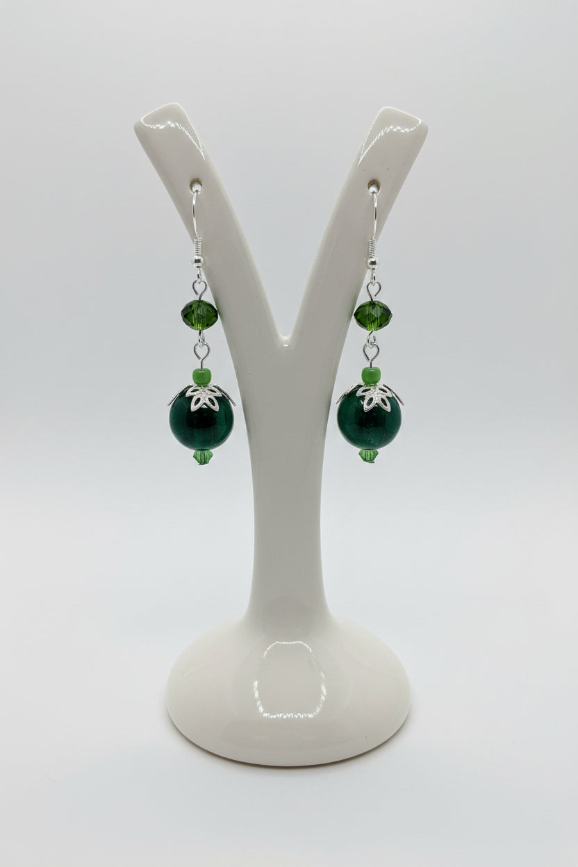 A pair of green beaded dangle earrings displayed on a white ceramic jewelry stand against a light gray background.