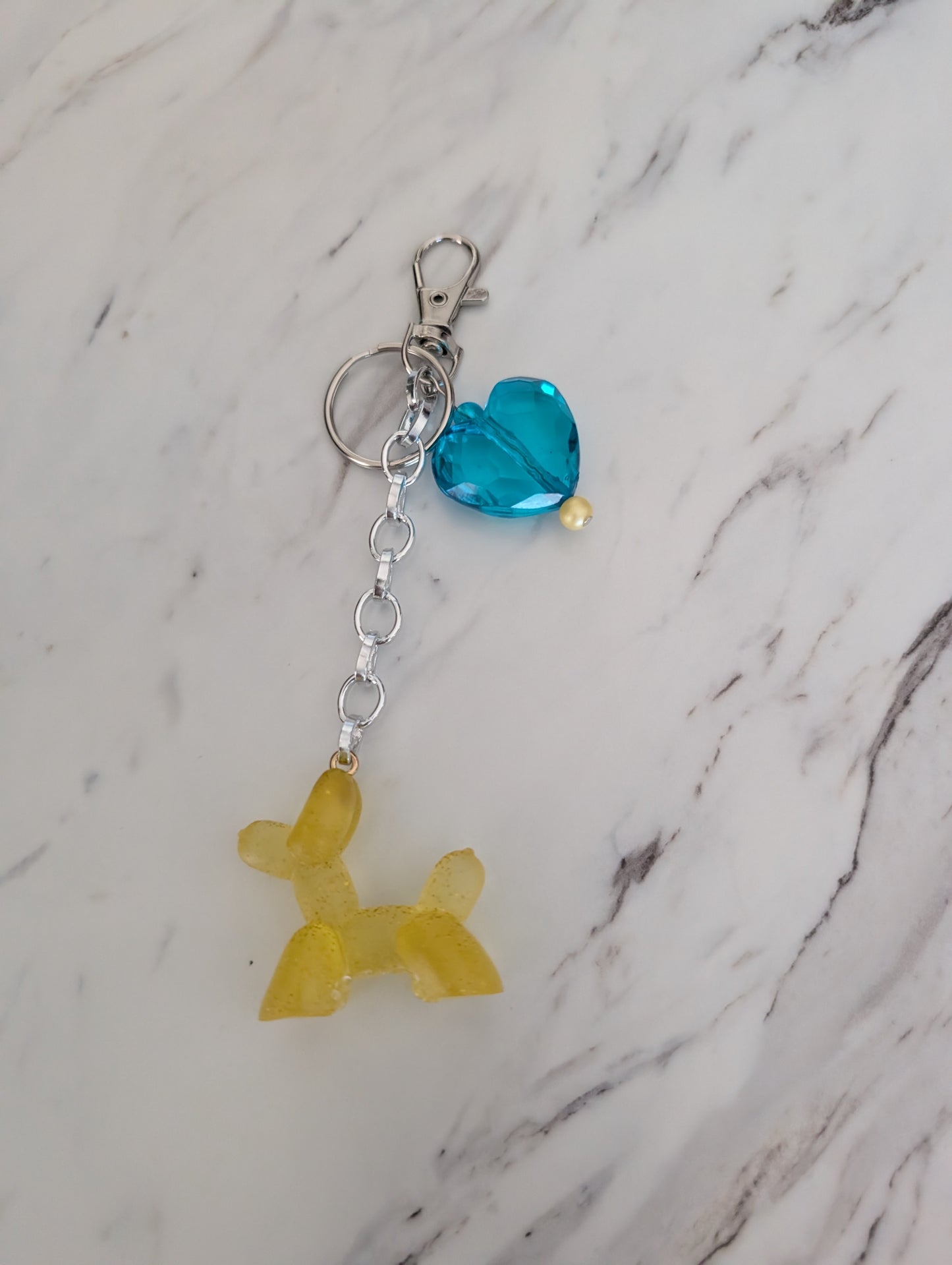 Keychain with a yellow dog-shaped charm and blue heart charm on a marble background