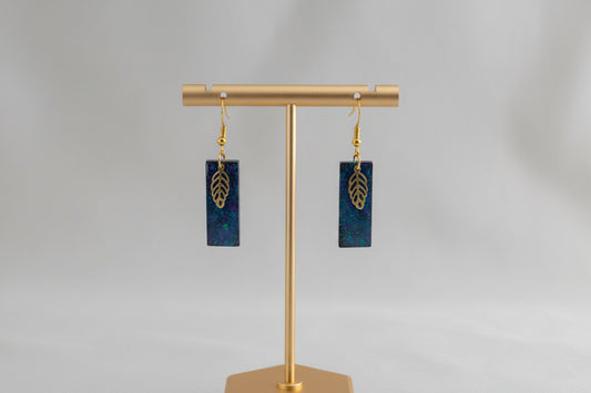 Pair of blue and gold earrings on a gold earring stand against a gray background