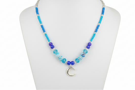 Necklace with blue beads and a moon charm on a mannequin bust.