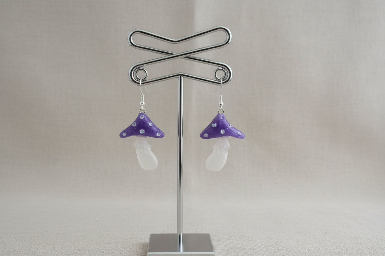Purple mushroom-shaped earrings on a stand against a gray background