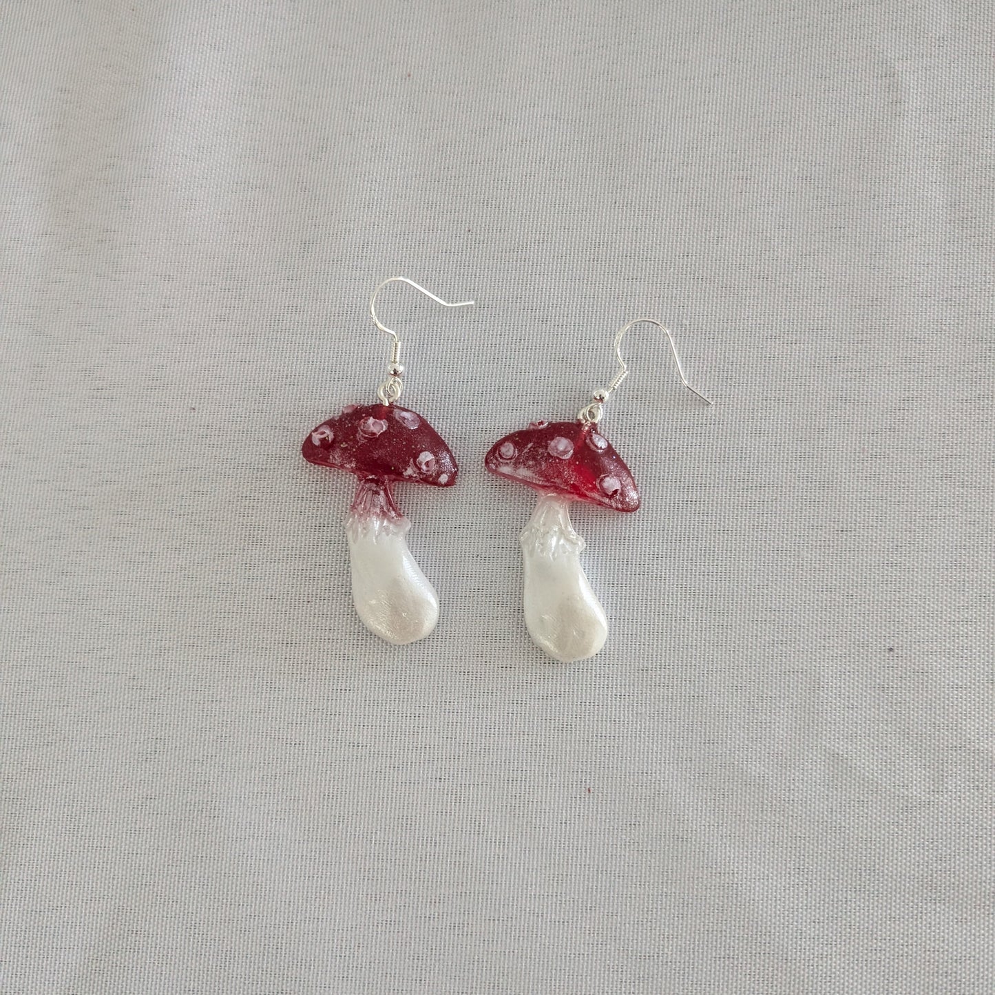 Mushroom-shaped earrings with red caps and white stems on a gray background