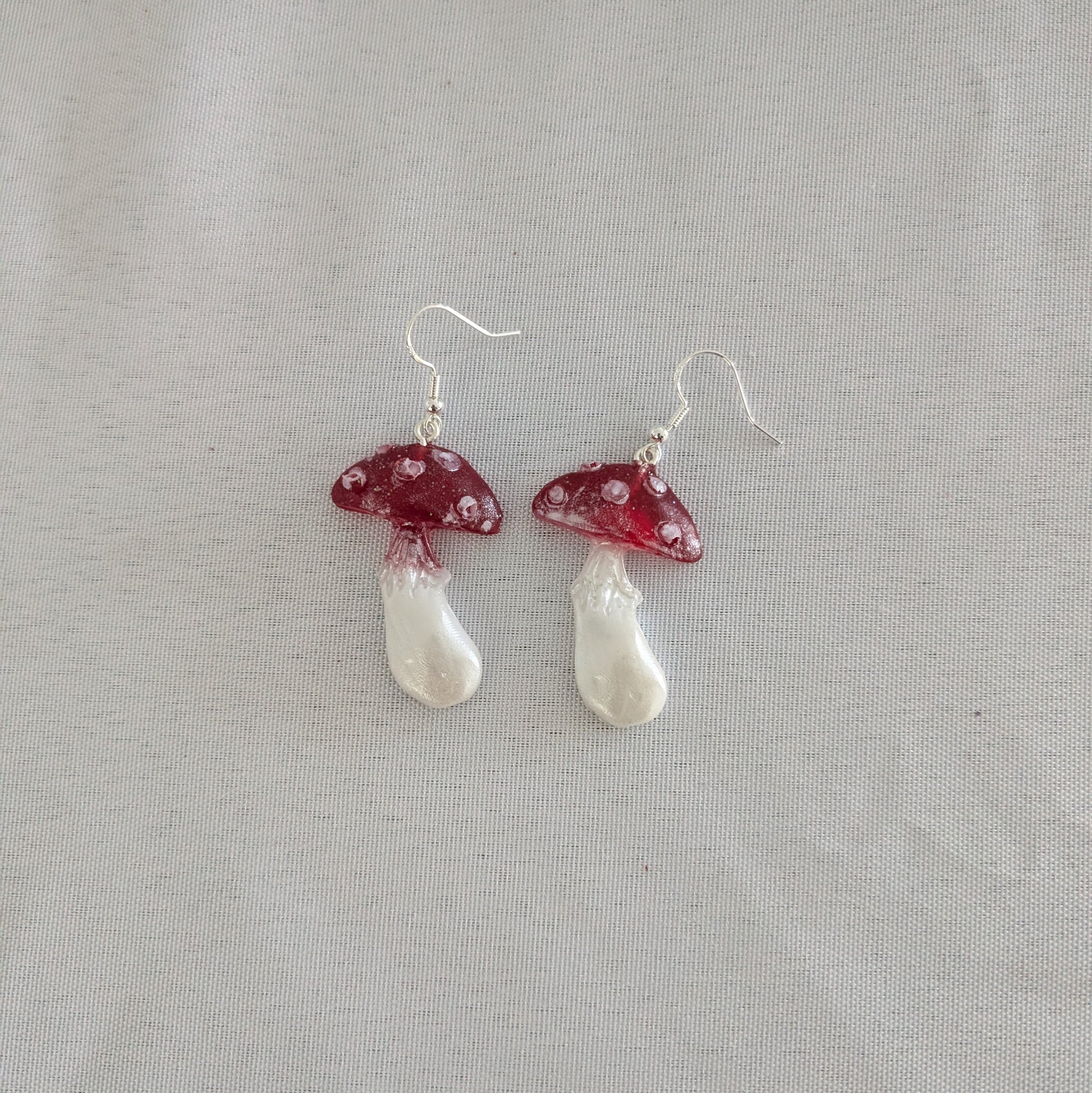 Mushroom-shaped earrings with red caps and white stems on a gray background