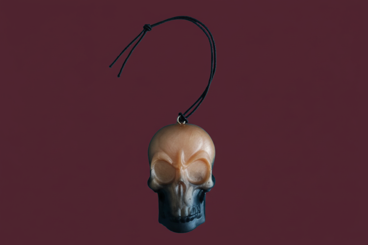 A resin skull face ornament with a black hanging cord, intended for use as a car decoration.