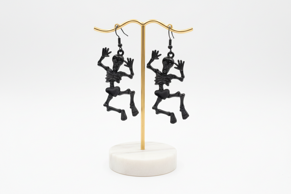 A pair of skeleton-shaped earrings in black, silver, and gold colors on hooks.