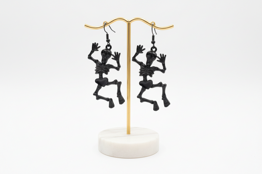 A pair of skeleton-shaped earrings in black, silver, and gold colors on hooks.